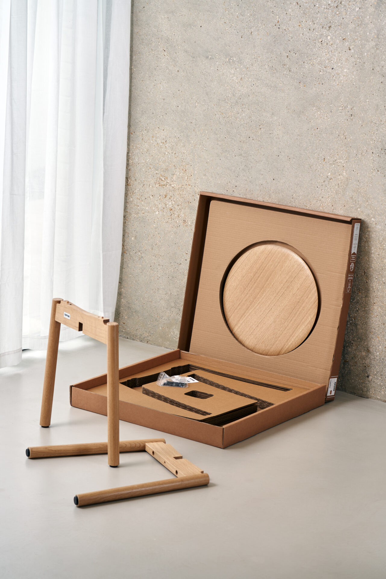 Flat-pack Tiptoe stool kit with wooden legs and circular seat partially assembled on the floor.