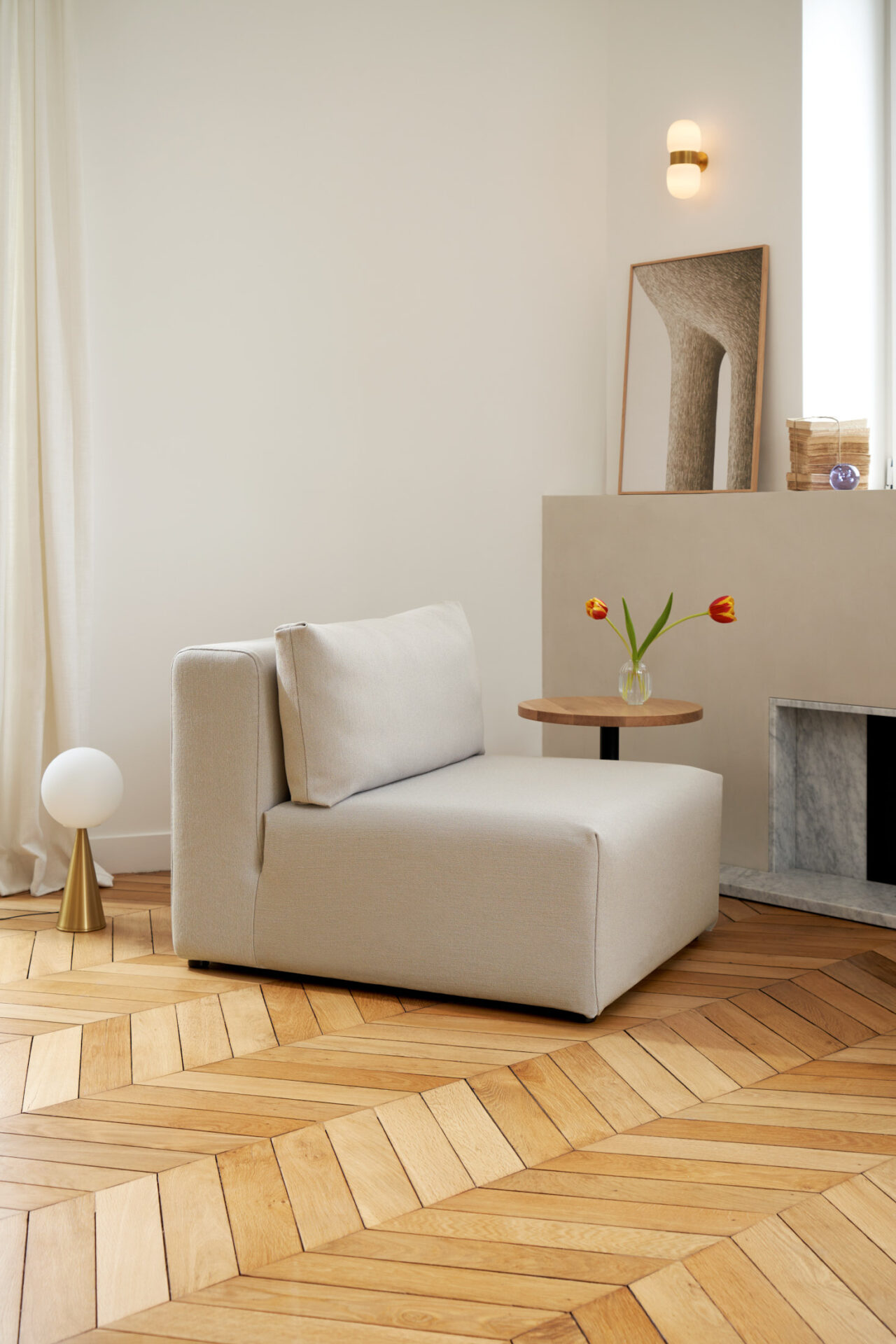 Modern living room corner with a beige Tiptoe modular sofa and small wooden side table on a herringbone floor.