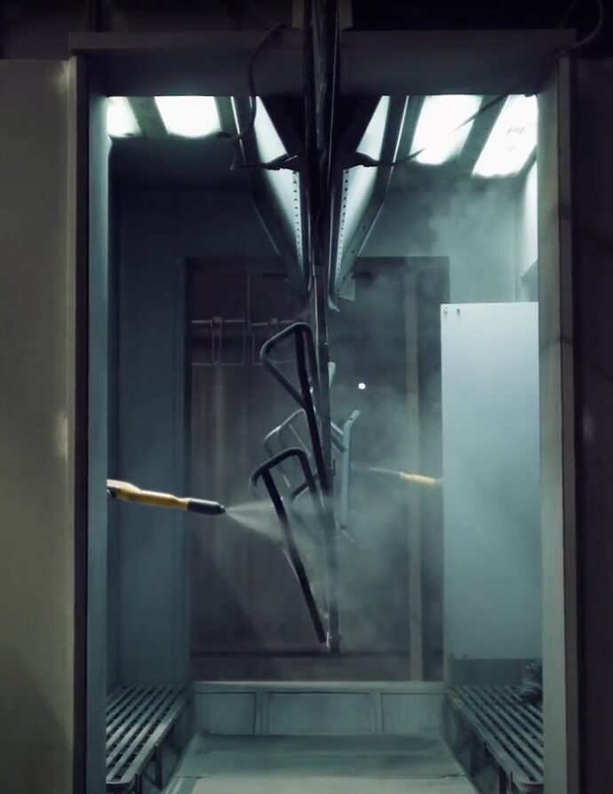 Metal chair frames being powder-coated in a manufacturing booth during Tiptoe’s production process.